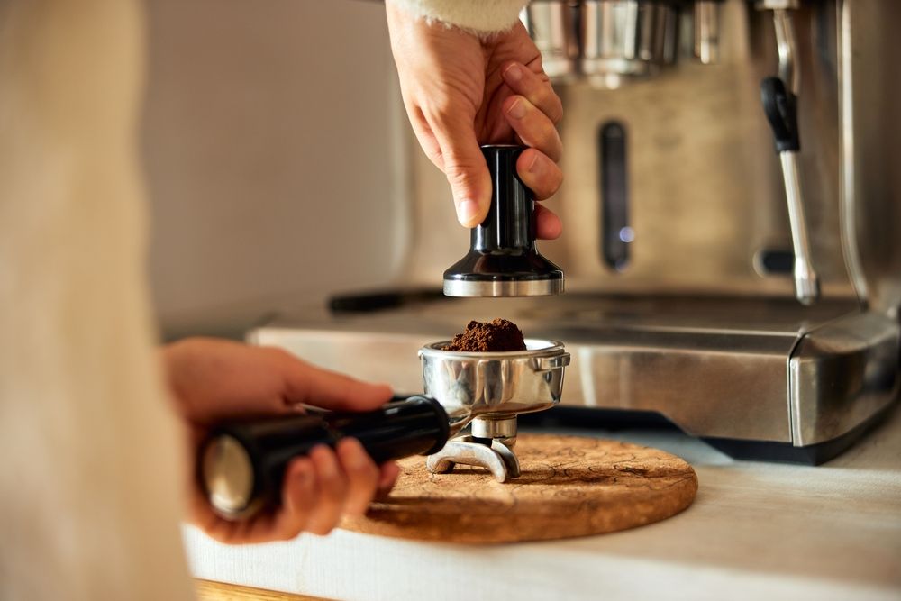 Barista tampira mlevenu kafu u portafilteru pre pripreme espressa